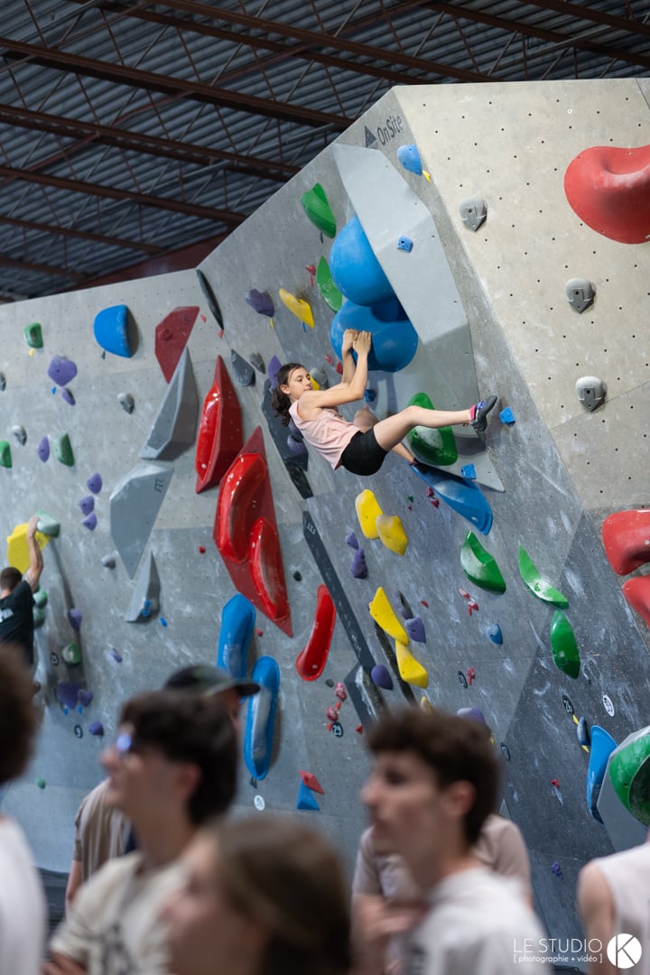 Jeune grimpeuse en plein mouvement sur un grand mur de blocs coloré